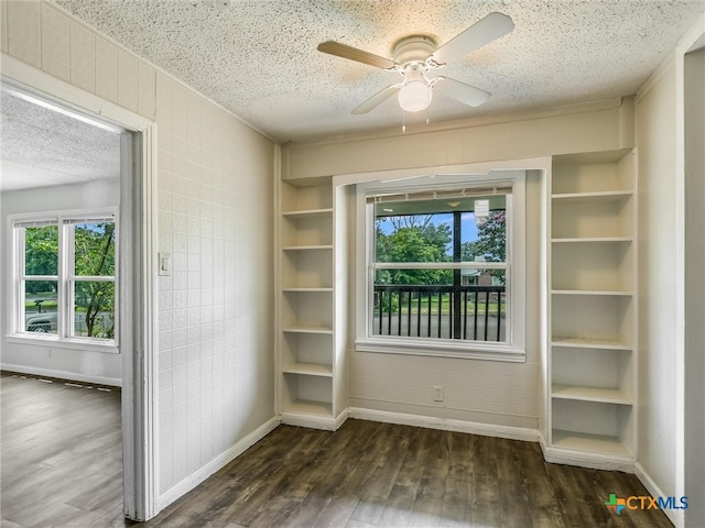 empty room featuring built in shelves, ceiling fan, dark wood-type flooring, and a textured ceiling