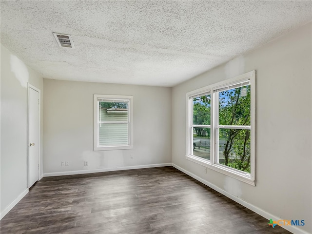 empty room with a textured ceiling, dark hardwood / wood-style floors, and plenty of natural light