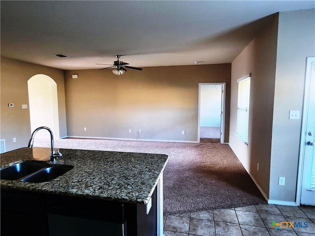 kitchen featuring dark stone counters, ceiling fan, sink, and light colored carpet