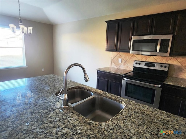 kitchen with sink, stainless steel appliances, dark stone counters, and a chandelier