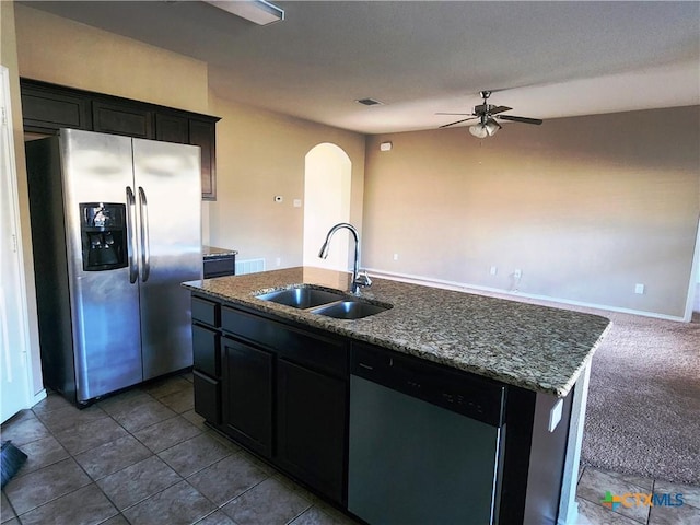 kitchen with a kitchen island with sink, sink, ceiling fan, appliances with stainless steel finishes, and stone countertops