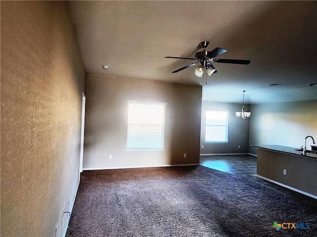 carpeted empty room featuring ceiling fan with notable chandelier