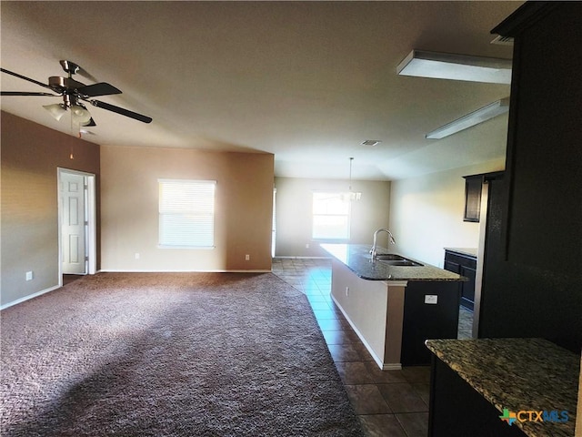 kitchen featuring light stone countertops, ceiling fan, sink, hanging light fixtures, and a center island with sink