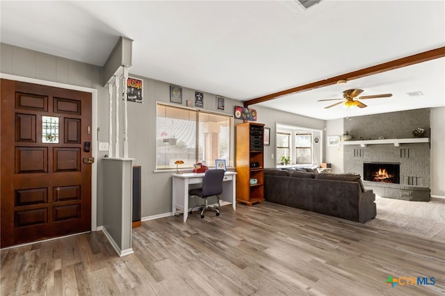 interior space with beam ceiling, ceiling fan, light hardwood / wood-style flooring, and a brick fireplace