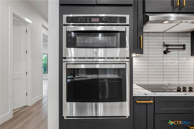 303 W Lane Ave, Manor, TX 78653 - kitchen with double oven, extractor fan, black electric stovetop, backsplash, and light wood finished floors