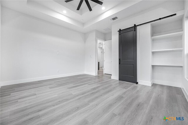 303 W Lane Ave, Manor, TX 78653 - unfurnished bedroom with a barn door, a raised ceiling, wood finished floors, recessed lighting, and a ceiling fan