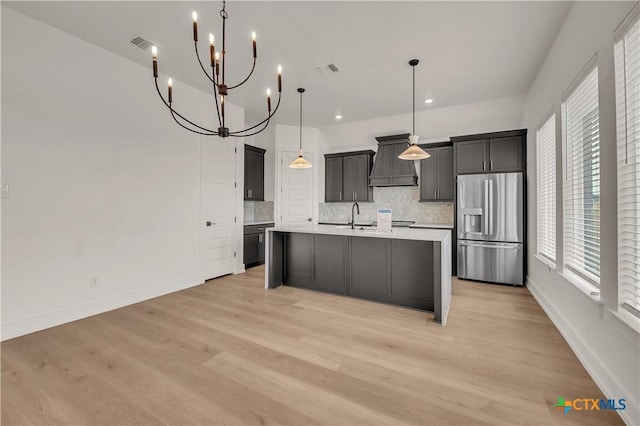 kitchen featuring decorative light fixtures, custom exhaust hood, light countertops, an island with sink, and stainless steel fridge with ice dispenser