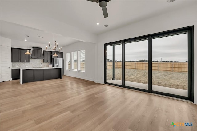 unfurnished living room with light wood finished floors, baseboards, visible vents, ceiling fan with notable chandelier, and recessed lighting