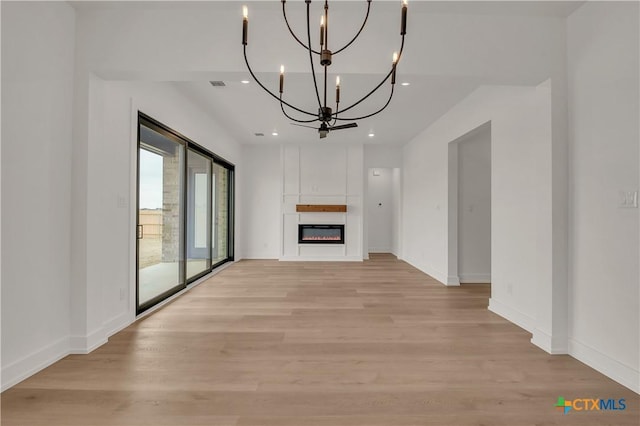 unfurnished living room featuring a chandelier, recessed lighting, baseboards, light wood finished floors, and a glass covered fireplace