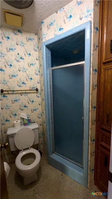 bathroom featuring a textured ceiling, toilet, and a shower with door