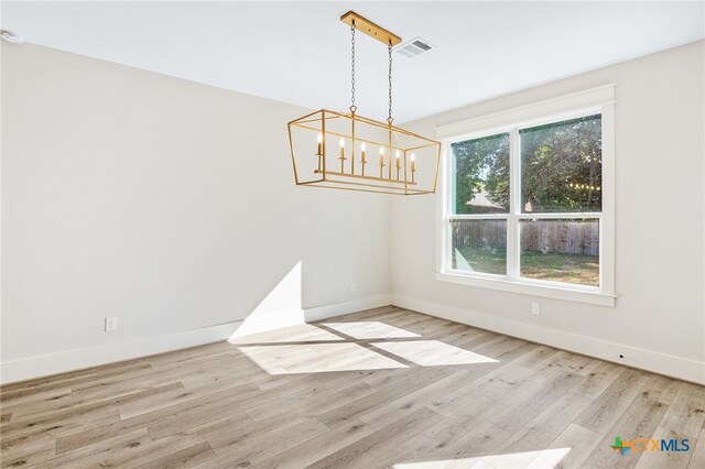 unfurnished room with light wood-type flooring and a notable chandelier