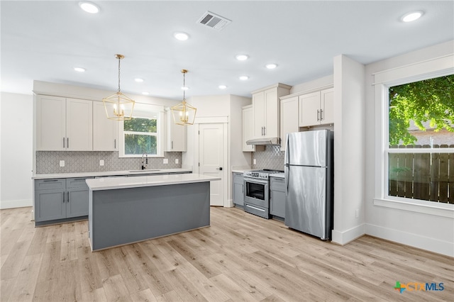 kitchen with gray cabinetry, stainless steel appliances, light wood-type flooring, decorative light fixtures, and sink