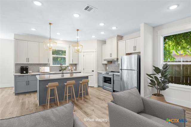 kitchen featuring stainless steel appliances, light hardwood / wood-style floors, gray cabinetry, and decorative light fixtures