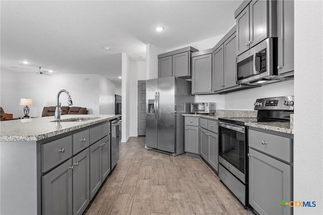 kitchen with gray cabinets, a sink, stainless steel appliances, light wood-style floors, and open floor plan