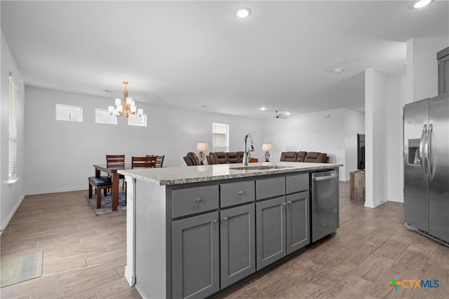 kitchen with wood finish floors, gray cabinetry, a center island with sink, a sink, and appliances with stainless steel finishes