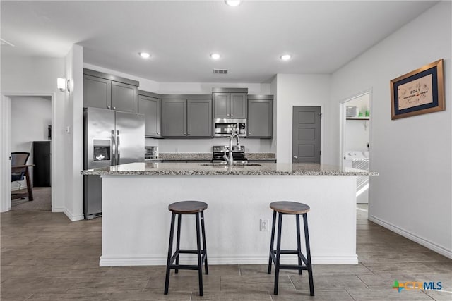 kitchen with light stone counters, appliances with stainless steel finishes, a kitchen breakfast bar, and a sink