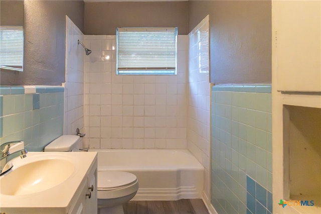 full bathroom with vanity, tiled shower / bath combo, hardwood / wood-style flooring, tile walls, and toilet