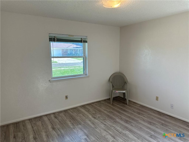 empty room with baseboards, a textured ceiling, and wood finished floors