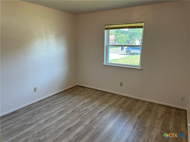 unfurnished room featuring a textured ceiling, baseboards, and wood finished floors
