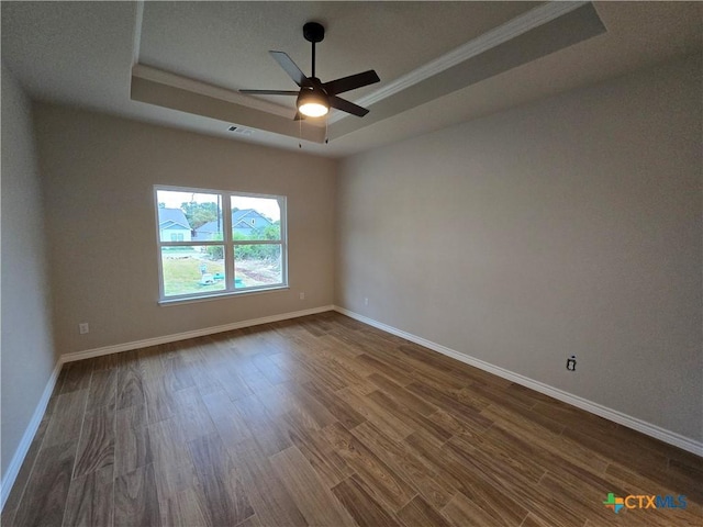 unfurnished room with a tray ceiling, ceiling fan, dark hardwood / wood-style floors, and ornamental molding