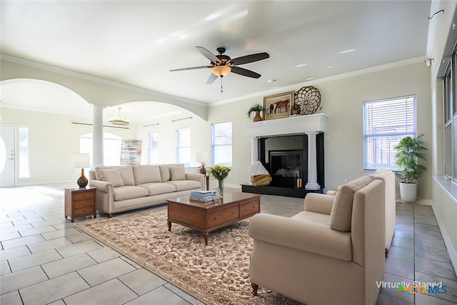 living area with light tile patterned floors, a ceiling fan, crown molding, and a glass covered fireplace