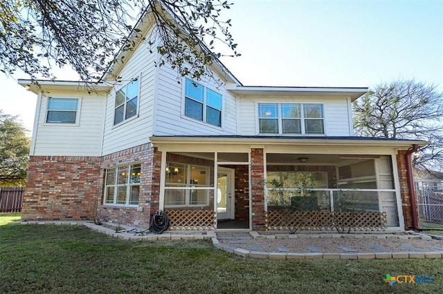 view of front facade featuring brick siding, a front lawn, fence, and a sunroom