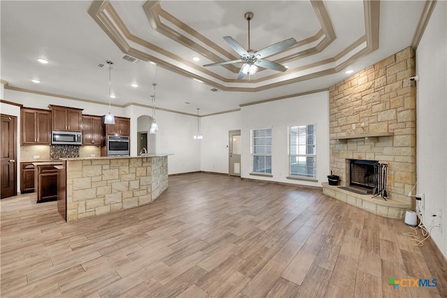 living room featuring light hardwood / wood-style floors, a raised ceiling, a stone fireplace, and crown molding