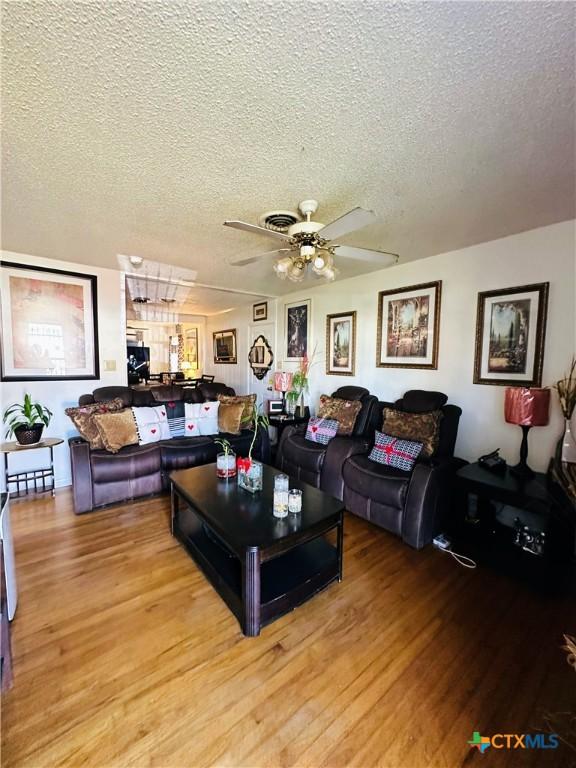 living room featuring ceiling fan, a textured ceiling, and wood finished floors