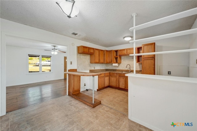 kitchen with ceiling fan, sink, light hardwood / wood-style flooring, kitchen peninsula, and a textured ceiling