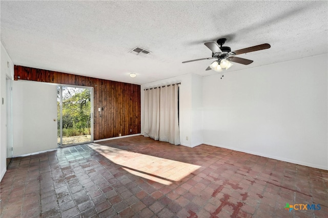 empty room featuring ceiling fan, wood walls, and a textured ceiling