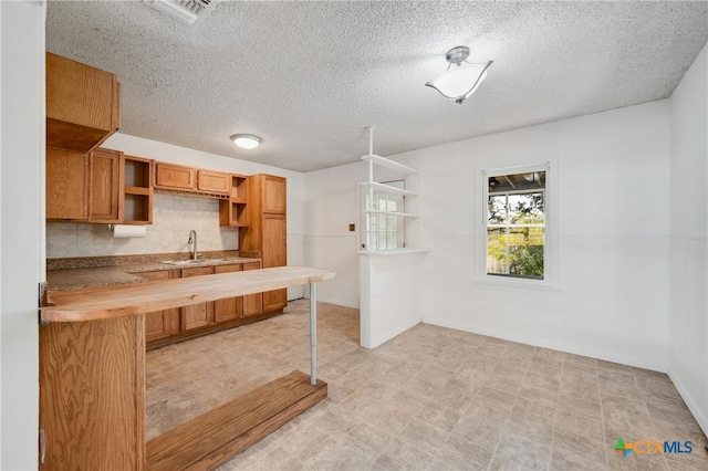 kitchen with sink, a textured ceiling, butcher block countertops, and backsplash