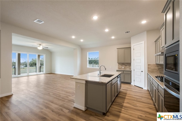 kitchen with light hardwood / wood-style floors, appliances with stainless steel finishes, sink, and a center island with sink