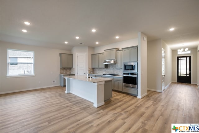 kitchen with gray cabinets, appliances with stainless steel finishes, a center island with sink, and light hardwood / wood-style flooring