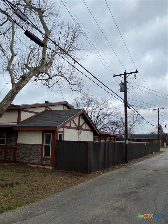 view of side of home featuring stone siding, fence, and stucco siding