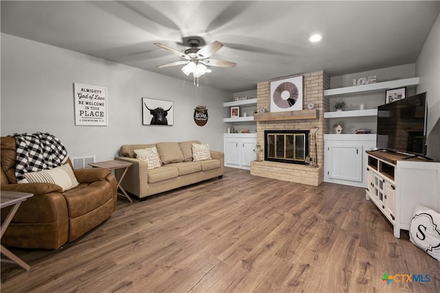 living room with ceiling fan, built in features, a fireplace, and hardwood / wood-style flooring