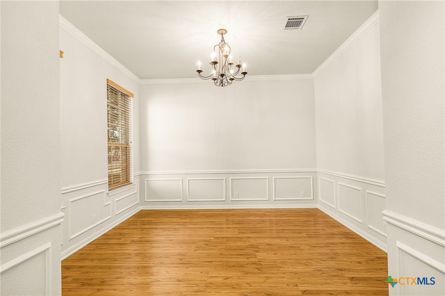 spare room with hardwood / wood-style floors, ornamental molding, and an inviting chandelier