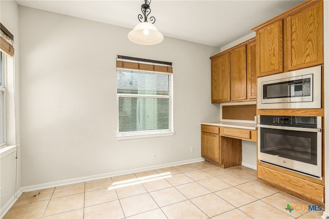 kitchen with light tile patterned flooring, built in desk, decorative light fixtures, and appliances with stainless steel finishes