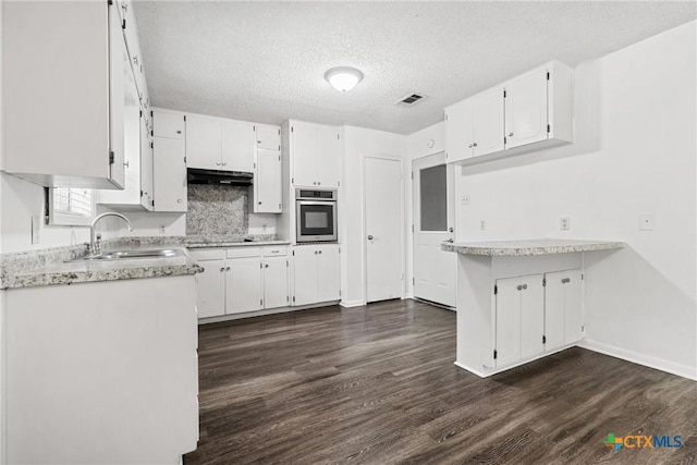 kitchen with stainless steel oven, white cabinets, sink, dark hardwood / wood-style floors, and a textured ceiling