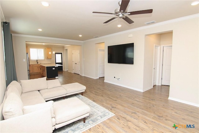 unfurnished living room with ceiling fan, sink, light wood-type flooring, and ornamental molding