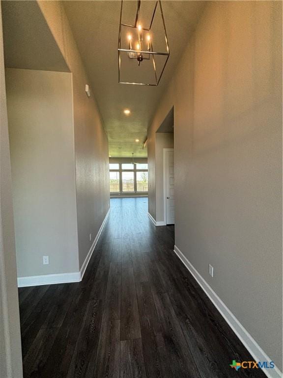 corridor featuring dark wood-type flooring, a notable chandelier, and baseboards