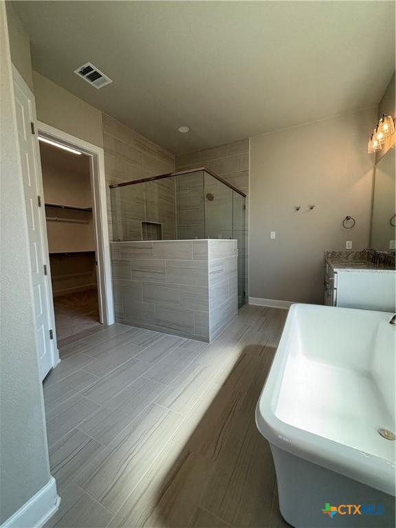 bathroom featuring visible vents, baseboards, a walk in closet, vanity, and a shower stall