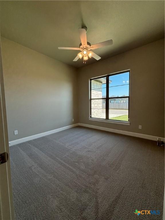 spare room featuring baseboards, dark carpet, and a ceiling fan