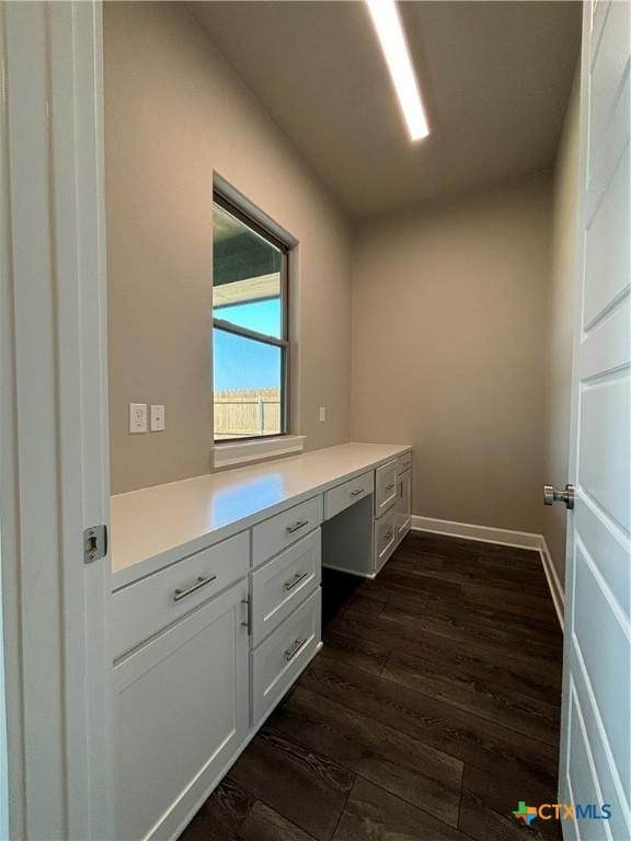 unfurnished office with dark wood-style floors, built in desk, and baseboards