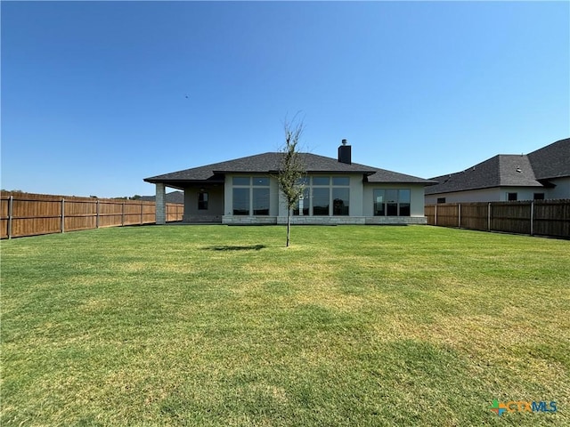 back of house with a fenced backyard, a chimney, and a yard