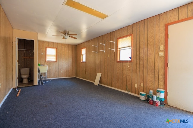 unfurnished room with wooden walls, ceiling fan, and dark carpet