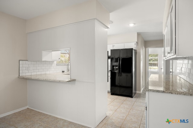 kitchen featuring plenty of natural light, black fridge, light stone countertops, and white cabinets