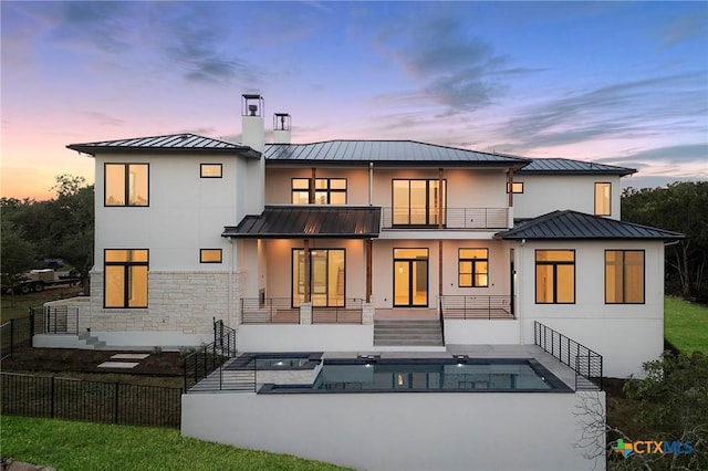 back house at dusk featuring a balcony, a patio area, and a pool with hot tub