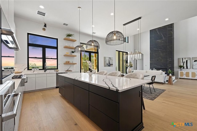 kitchen featuring white cabinets, a spacious island, light hardwood / wood-style flooring, decorative light fixtures, and a kitchen bar