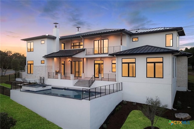 back house at dusk with a swimming pool with hot tub and a balcony