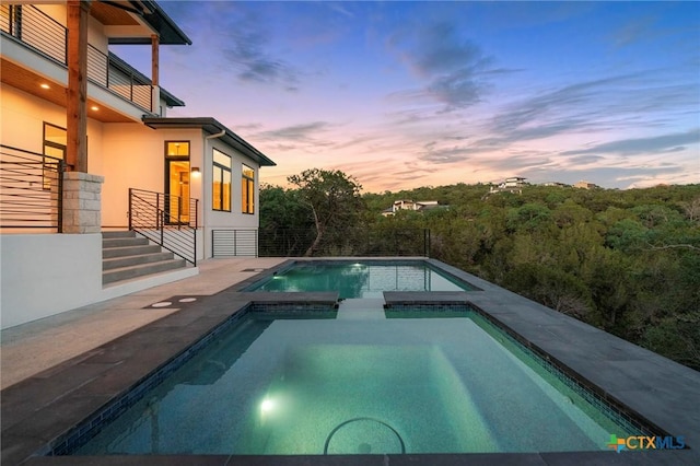 pool at dusk with an in ground hot tub